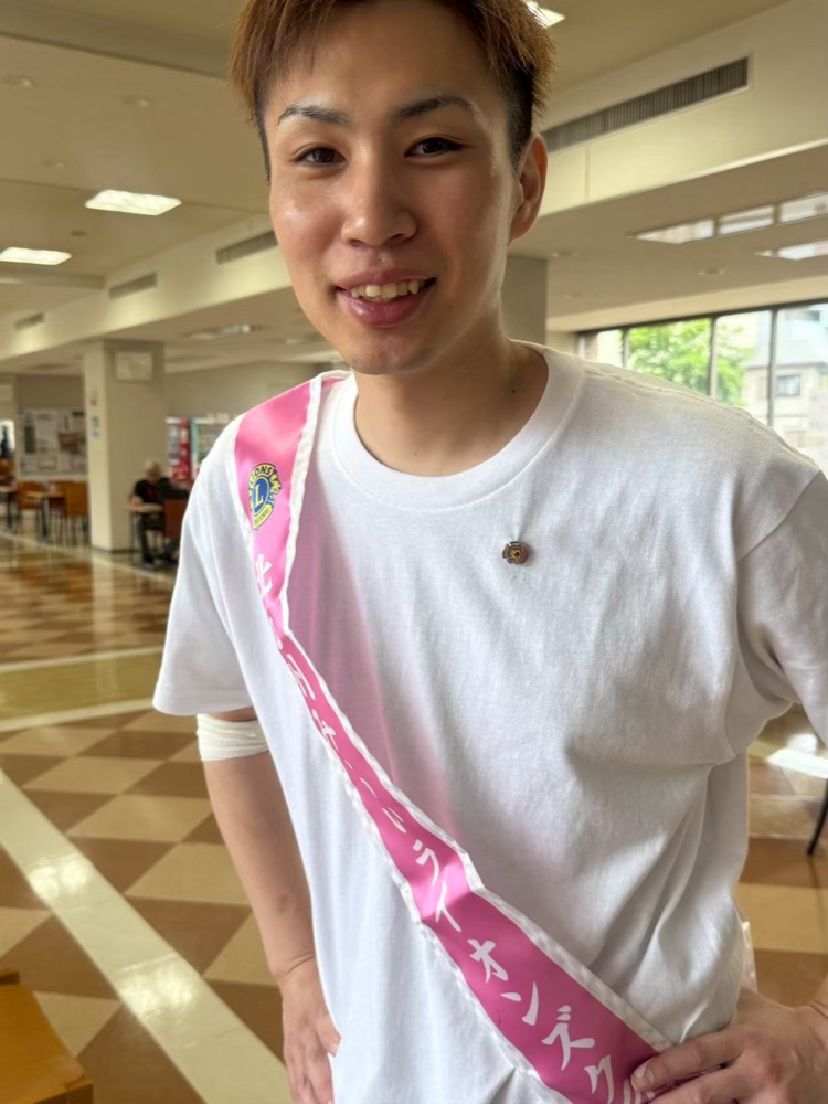 献血のタスキをかけて呼びかける学生の笑顔